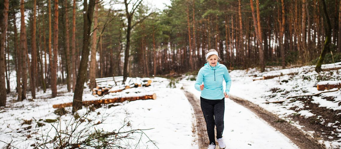 Happy senior woman jogging in winter nature.